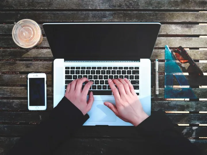 Hands typing on a laptop next to a smartphone